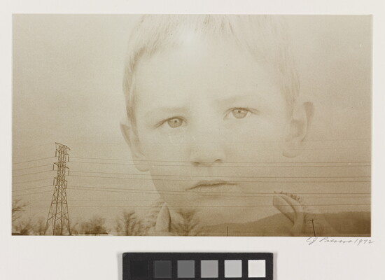 A sepia-toned double-exposed photograph of the face of a young White child over a landscape of powerlines and hills.