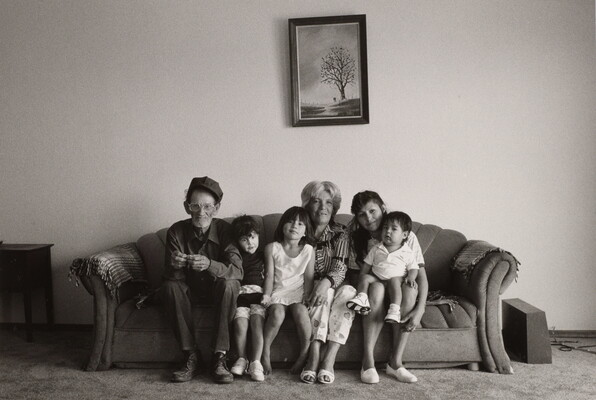 A black-and-white photograph of an older man and woman, a younger woman, and three children seated together on a sofa.