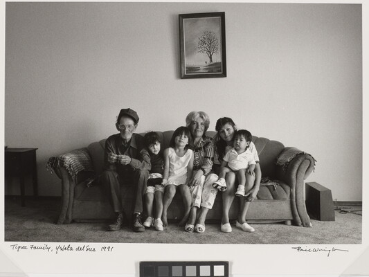 A black-and-white photograph of an older man and woman, a younger woman, and three children seated together on a sofa.