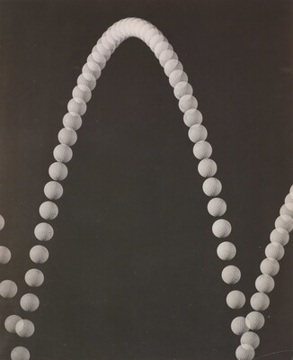 A black-and-white photograph of an upward arc made of white circles that resembles a sting of pearls on a black background.