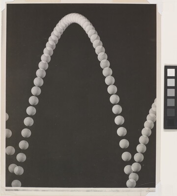 A black-and-white photograph of an upward arc made of white circles that resembles a sting of pearls on a black background.