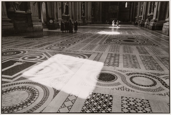 A black-and-white photograph of a square of sunlight on an ornate mosaic floor.