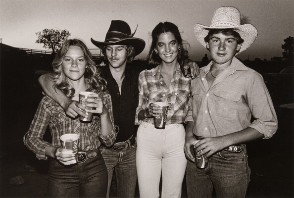 A black-and-white photograph of White teenagers, two girls and two boys with their arms around each other, holding Coca-Cola cups and wearing western clothing.