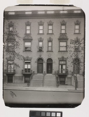 A black-and-white photograph of the facades of three-story row homes with steps leading to front doors.
