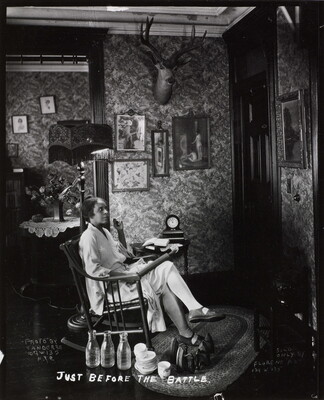 A black-and-white photograph of a Black woman in a rocking chair, holding a rolling pin on her lap, waiting at a front door.