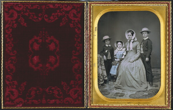 A hand-painted black-and-white formal portrait photograph in a gold frame of a White woman sitting with two boys and a girl standing around her.