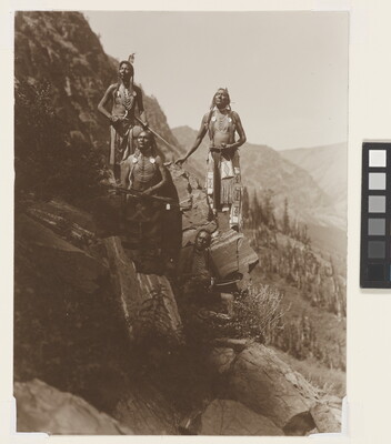 A sepia-toned photograph of four Native Americans in traditional dress arranged on a steep, rocky slope.
