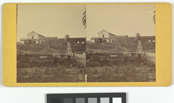 Two almost identical sepia-toned photographs side by side an adobe building on a hill with a windmill in the foreground.
