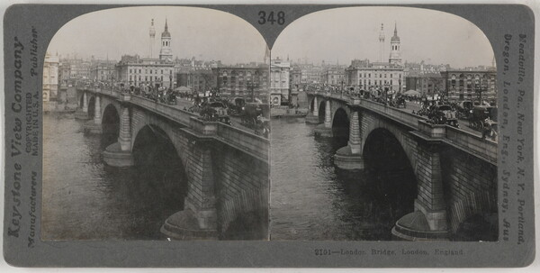 Two almost identical side-by-side black-and-white photographs of a brick arch bridge that spans a river, pedestrians and cars on top, and a city skyline in the background.