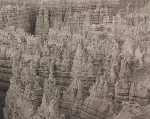 A black-and-white landscape photograph of banded rock formations in a canyon.