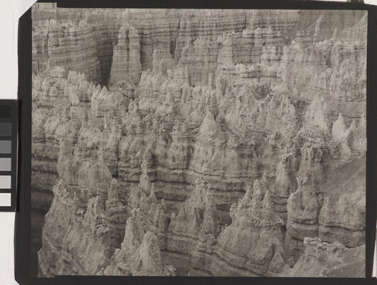 A black-and-white landscape photograph of a view of banded rock formations in a canyon.
