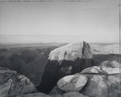 A black-and-white photograph of large rock formations and shadows cast on them, including the silhouette of a person.