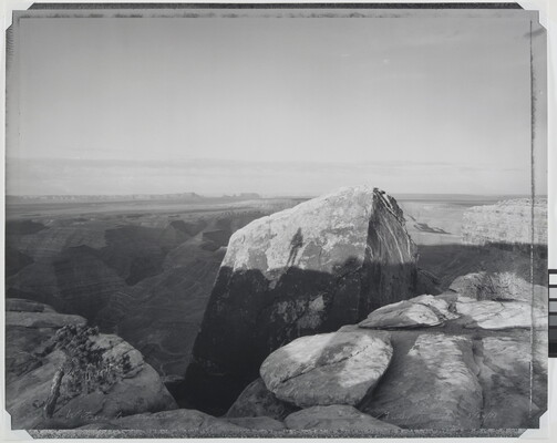 A black-and-white photograph of large rock formations and shadows cast on them, including the silhouette of a person.