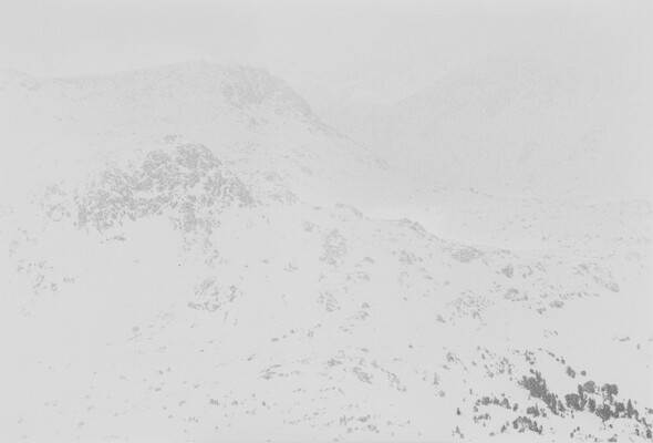 A black-and-white photograph of a snowy mountain with snow and clouds slightly obscuring the view.