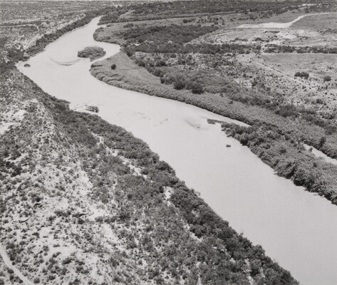 A black-and-white aerial photograph of a river, both shores dotted with trees and shrubs.