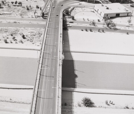 A black-and -white aerial photograph of a bridge that spans across a river.