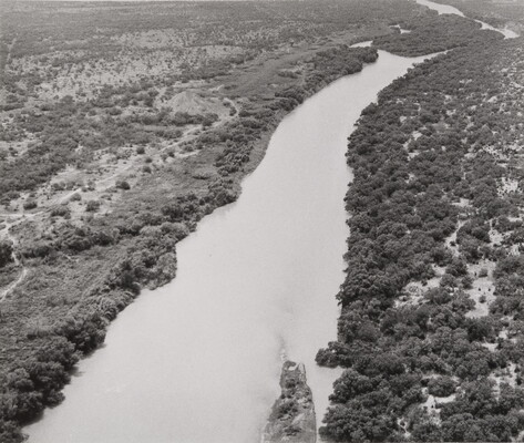 A black-and-white aerial photograph of a river with trees on both sides of its banks.