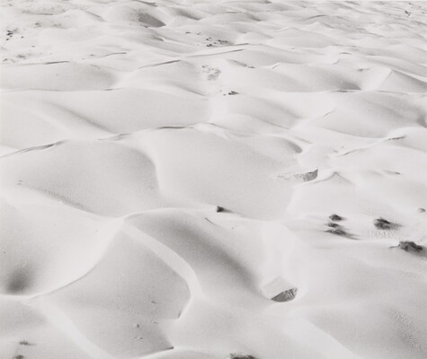 A black-and-white photograph of gentle ripples and waves in the desert sand.