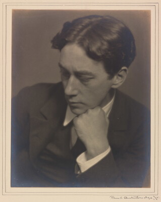 A sepia-toned photograph of a young White man wearing a dark suit, resting his chin on his fist, looking down to his right.