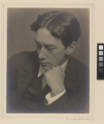 A sepia-toned photograph of a young White man wearing a dark suit, resting his chin on his fist, looking down to his right.