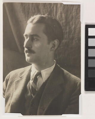 A sepia-toned photograph of a White man with a moustache wearing a dark suit, white shirt, and striped tie looking to the side.