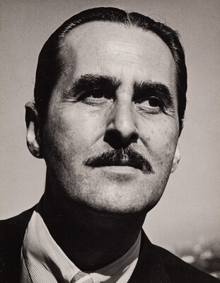 A black-and-white photograph of a White man with slicked back dark hair and a mustache.
