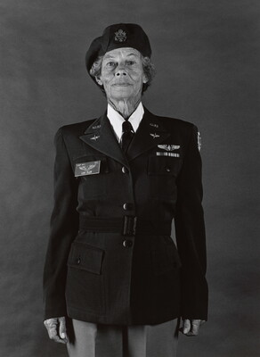 A black-and-white photograph of an older White woman with a wrinkled face wearing a beret and military uniform, standing straight and looking at the viewer.