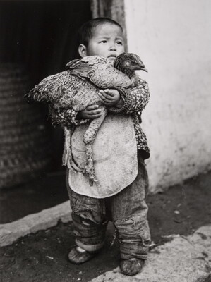 A black-and-white photograph of a Chinese toddler holding a chicken in his arms.
