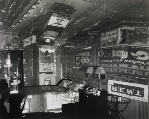 A black-and-white photograph of a bedroom covered with reflections and lights from the signs and advertisements outside.
