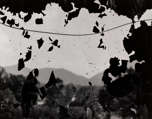 A black-and-white photograph of hills as seen through what looks like a cracked window covered with flecks of black paint.