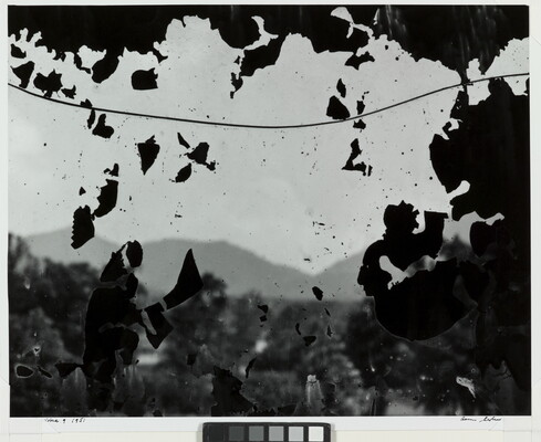 A black-and-white photograph of hills as seen through what looks like a cracked window covered with flecks of black paint.