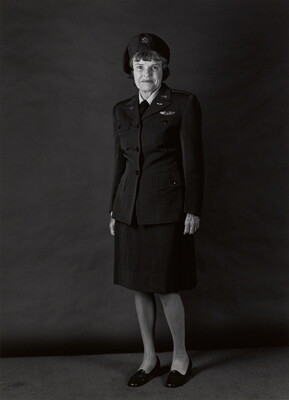 A black-and-white portrait photograph, in full length, of an older White woman wearing a military uniform that includes hat, jacket, and skirt.
