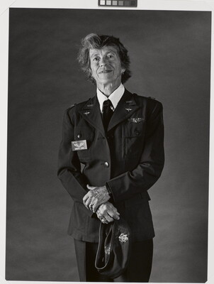 A black-and-white portrait photograph of an older White woman with short hair wearing a WASP military uniform and her hands in front of her holding a hat.