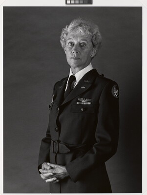 A black-and-white portrait photograph of a middle-aged White woman with curly hair wearing a WASP military uniform and her hands folded in front of her.