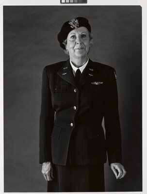 A black-and-white portrait photograph of an older White woman wearing a beret with an insignia on the front, a WASP military uniform, and holding her hands at her sides.