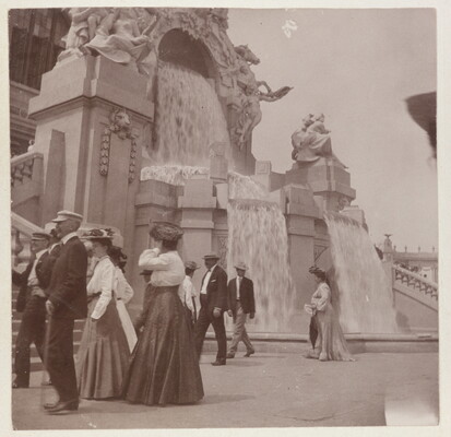A sepia-toned photograph of women in long skirts and men in hats and jackets strolling by an elaborately sculpted facade with waterfalls.