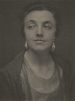A sepia-toned portrait photograph of a White woman, hair tied back to show her dangling earrings.