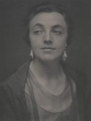 A sepia-toned portrait photograph of a White woman, hair tied back to show her dangling earrings.