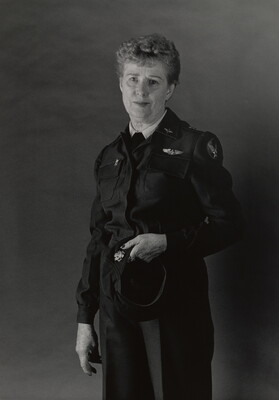 A black-and-white portrait photograph of an older White woman with short gray hair wearing an Air Force uniform, holding her hat in one hand.