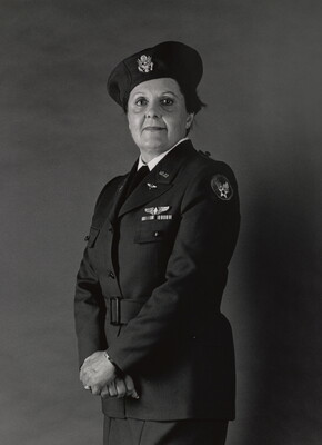 A black-and-white portrait photograph of a middle-aged White woman wearing an Air Force uniform, including a beret, hands crossed at her hips.