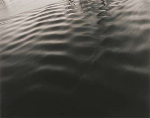 A black-and-white photograph of rippled water and bright reflections on the edges, taken at an angle.