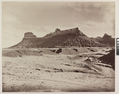 A sepia-toned photograph of a desert landscape with a rocky mesa in the distance.
