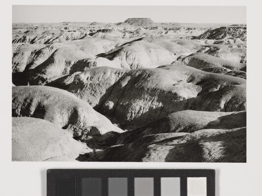 A black-and-white landscape photograph of sunlight on large, round desert rock formations.