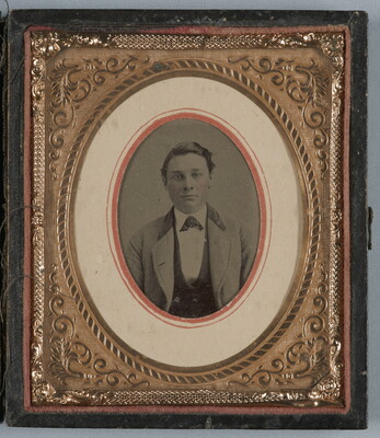An oval, black-and-white photograph in a decorative gold frame of a well-dressed White man wearing a three-piece suit.