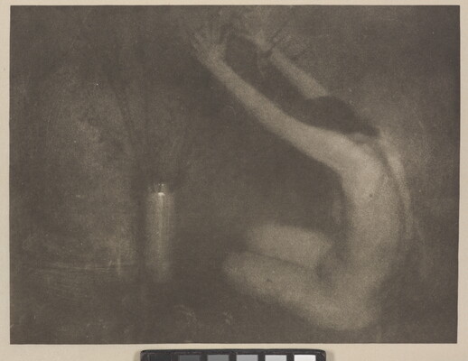 A soft-focus, black-and-white photograph of a nude White woman sitting on the floor next to a vase, her arms raised toward the flowers.