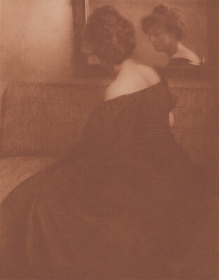 A sepia-toned photograph of a seated White woman, viewed from the side, wearing a long off-the-shoulder dress; her face is visible in the mirror she looks into.