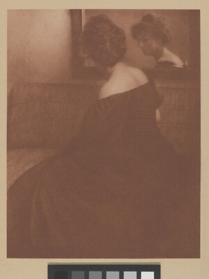 A sepia-toned photograph of a seated White woman, viewed from the side, wearing a long off-the-shoulder dress; her face is visible in the mirror she looks into.