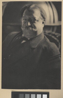 A sepia-toned portrait photograph of a White man with a curled mustache wearing a suit jacket and tie.