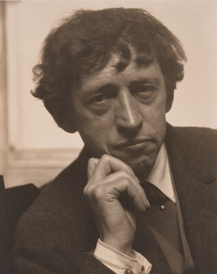 A sepia-toned photograph of a middle-aged White man, tousled hair, chin resting on one hand, wearing a suit and tie.