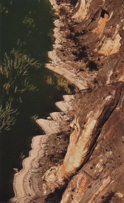 A color photograph of a landscape where a river meets a cliff face as viewed from above.